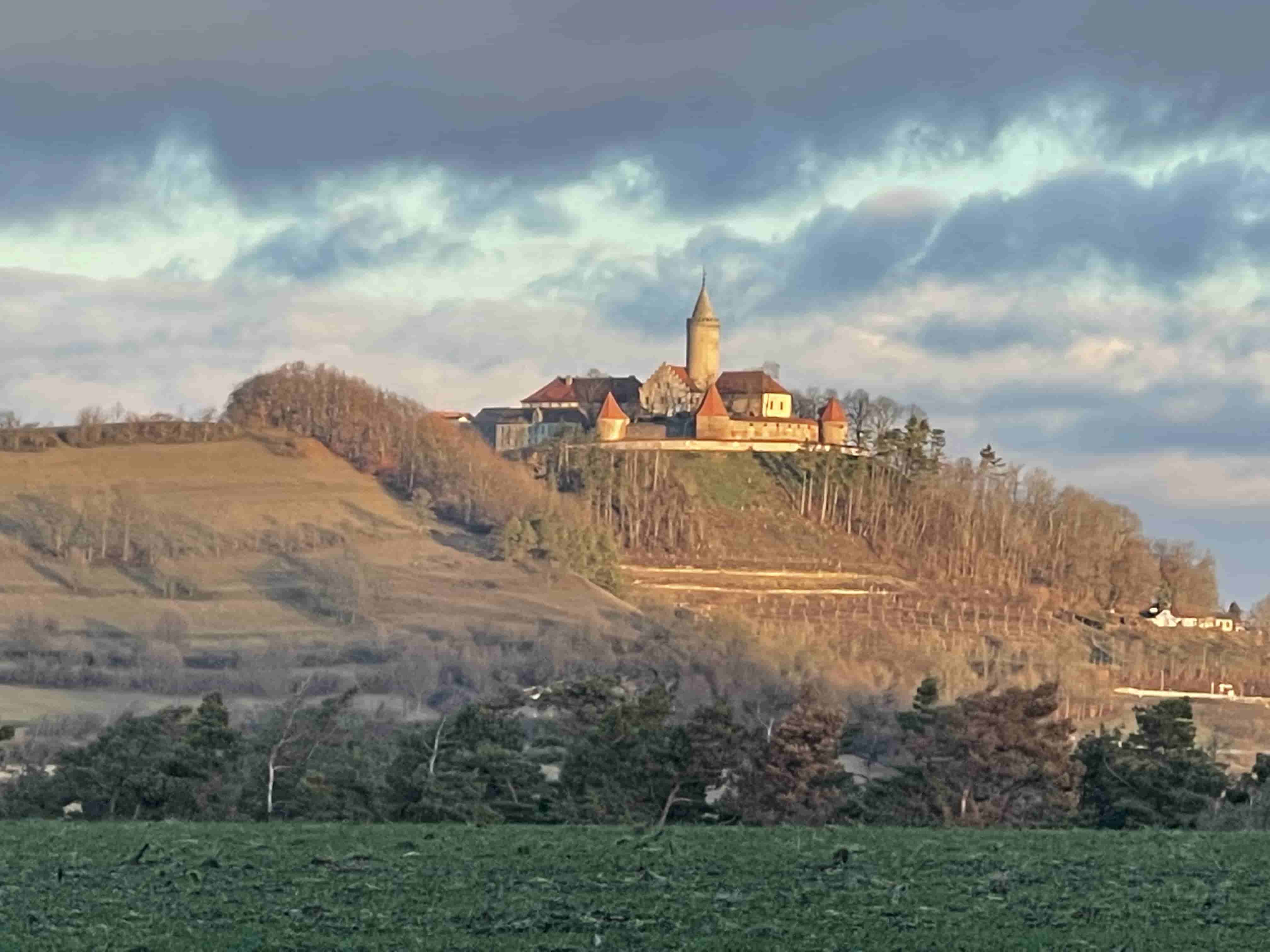 Burg Leuchtenburg thront auf einem bewaldeten Hügel unter einem bewölkten Himmel bei Sonnenuntergang.