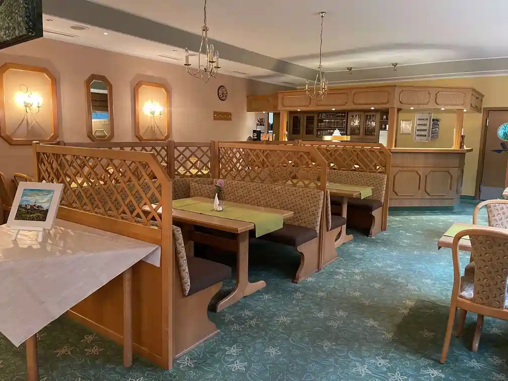 Gemütlicher Restaurantinnenraum mit Holzbänken, Tischen, Kronleuchtern und retro Teppichboden.