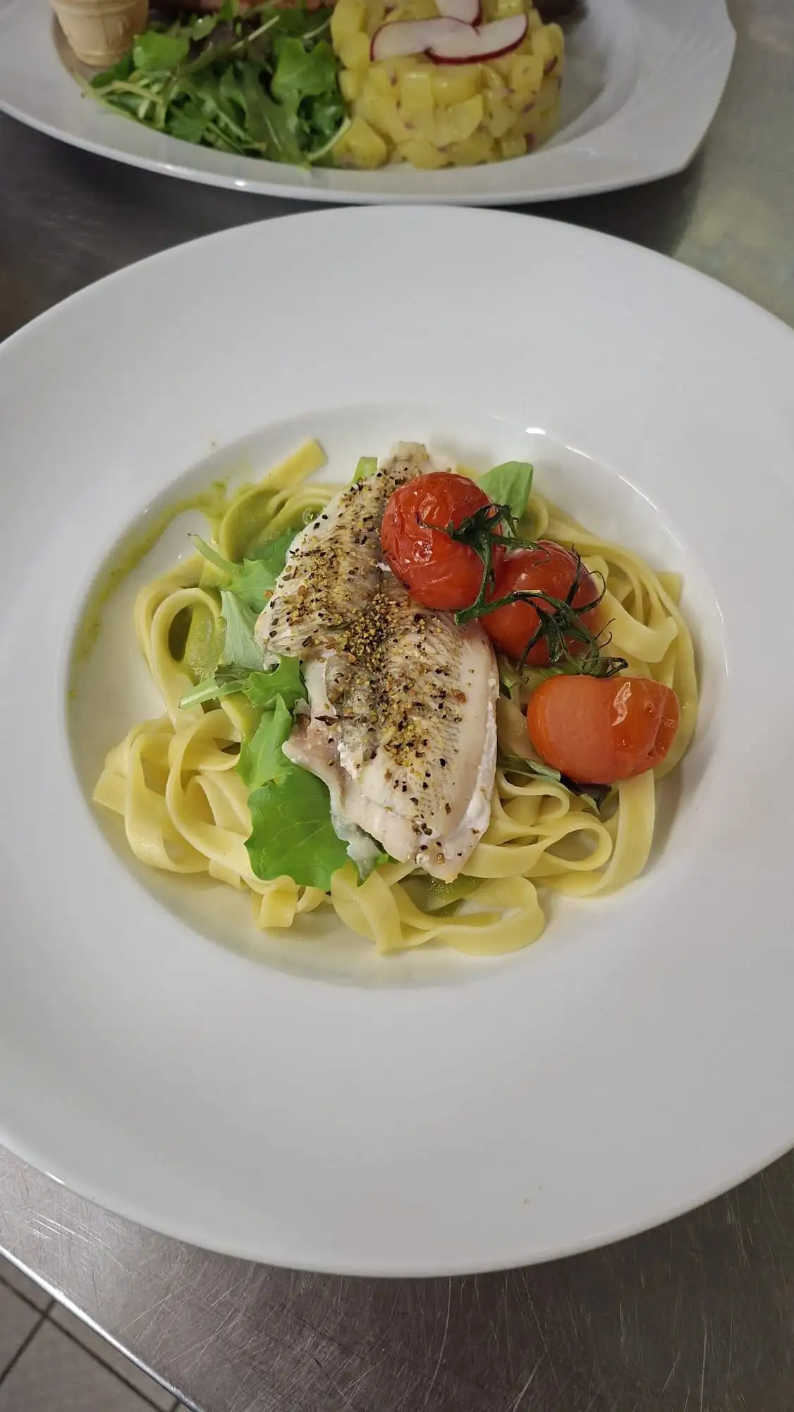 Tagliatelle mit gebratenem Fischfilet, Rucola und gerösteten Kirschtomaten auf weißem Teller.